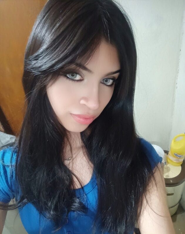 Close-up portrait of a woman with long black hair, blue eyes, and pink lips, wearing a blue top and looking at the camera.